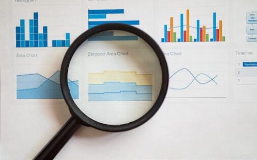 A magnifying glass focuses on various business charts and graphs on paper.